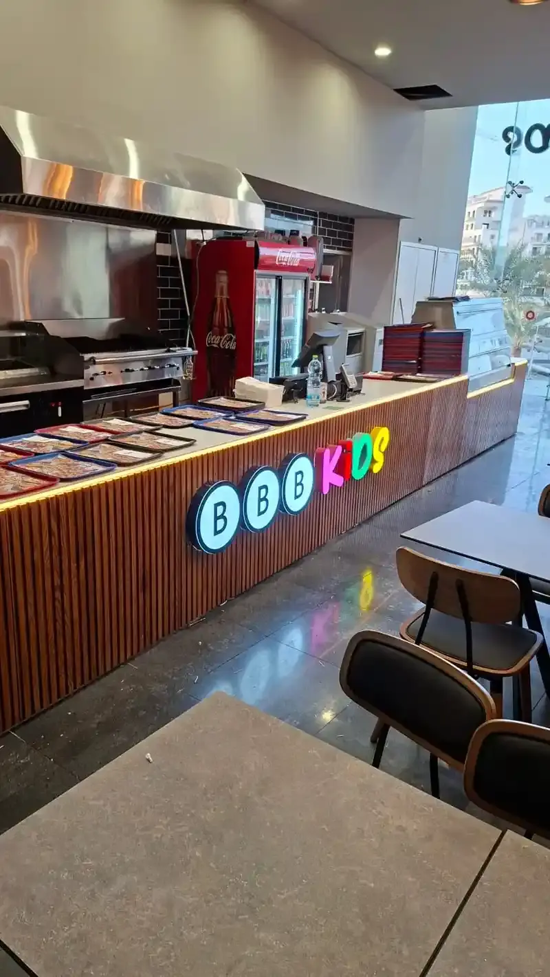 Letras interiores iluminadas montadas sobre un mostrador de listones de madera en un restaurante, con la cocina detrás