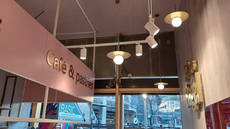 Letras doradas en relieve Café y pastries sobre un panel de pared rosado bajo lámparas colgantes en una cafetería