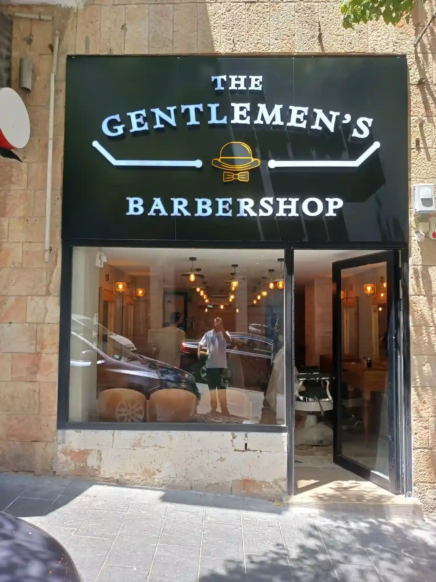 Rótulo comercial profesional para The Gentlemen's Barbershop — fachada oscura con letras iluminadas