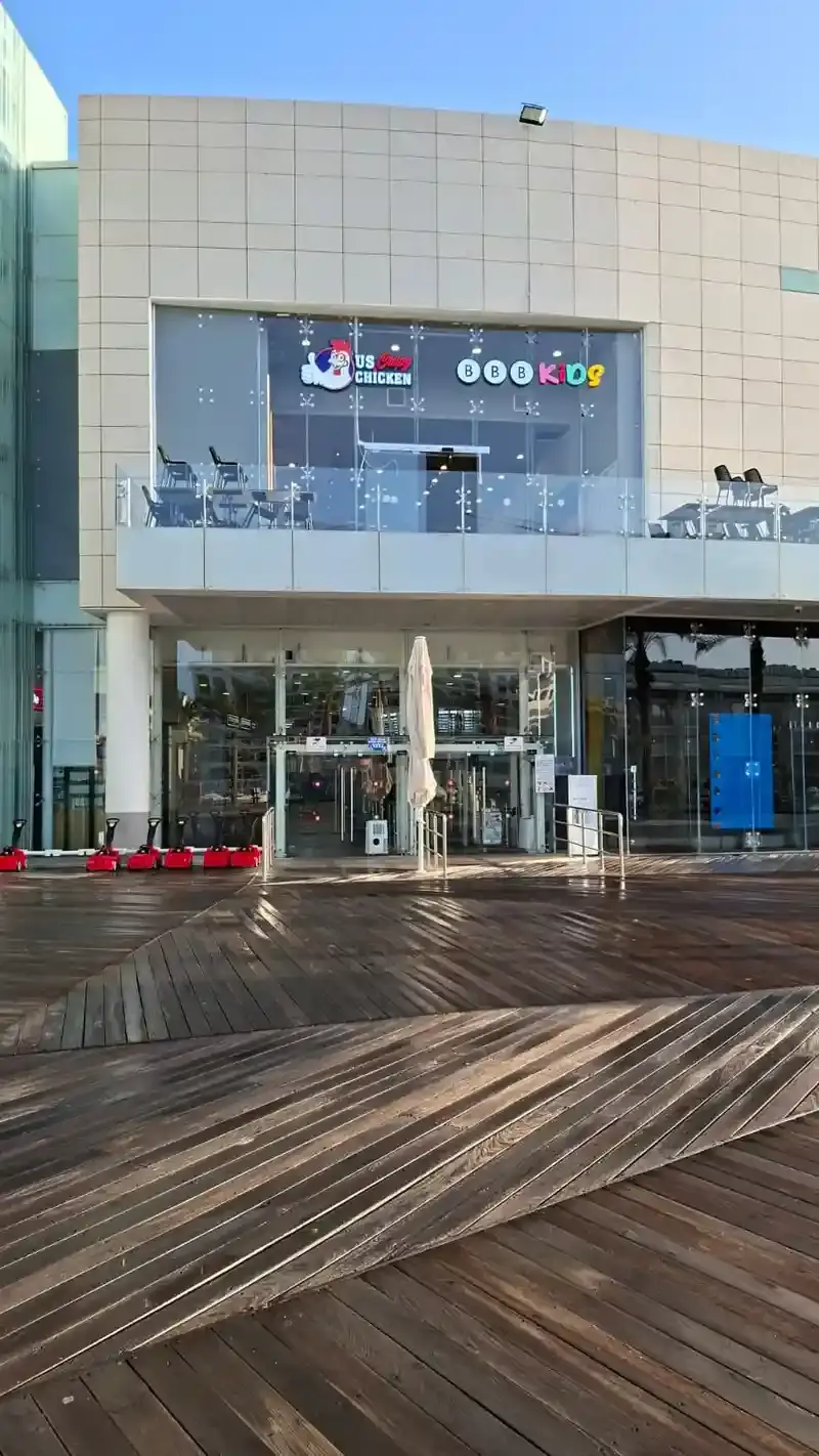 Rótulos iluminados en la fachada de vidrio superior de un edificio comercial de dos pisos sobre un paseo de madera