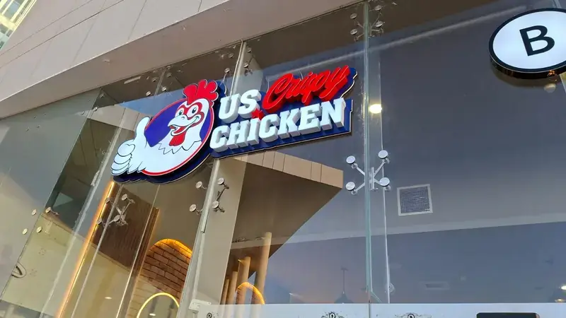 Letras de canal 3D iluminadas al frente y un logo de gallo sobre la entrada de vidrio de una tienda
