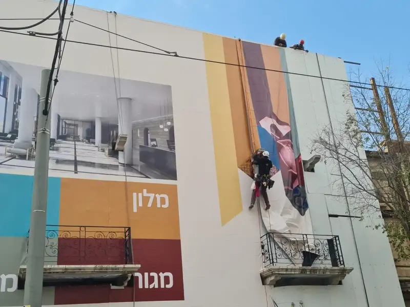 Instaladores en cuerdas colocando un rótulo del tamaño del edificio